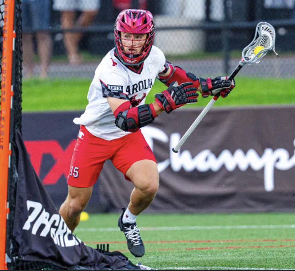 Lacrosse player in white Maryland jersey running on field holding lacrosse stick with ball.