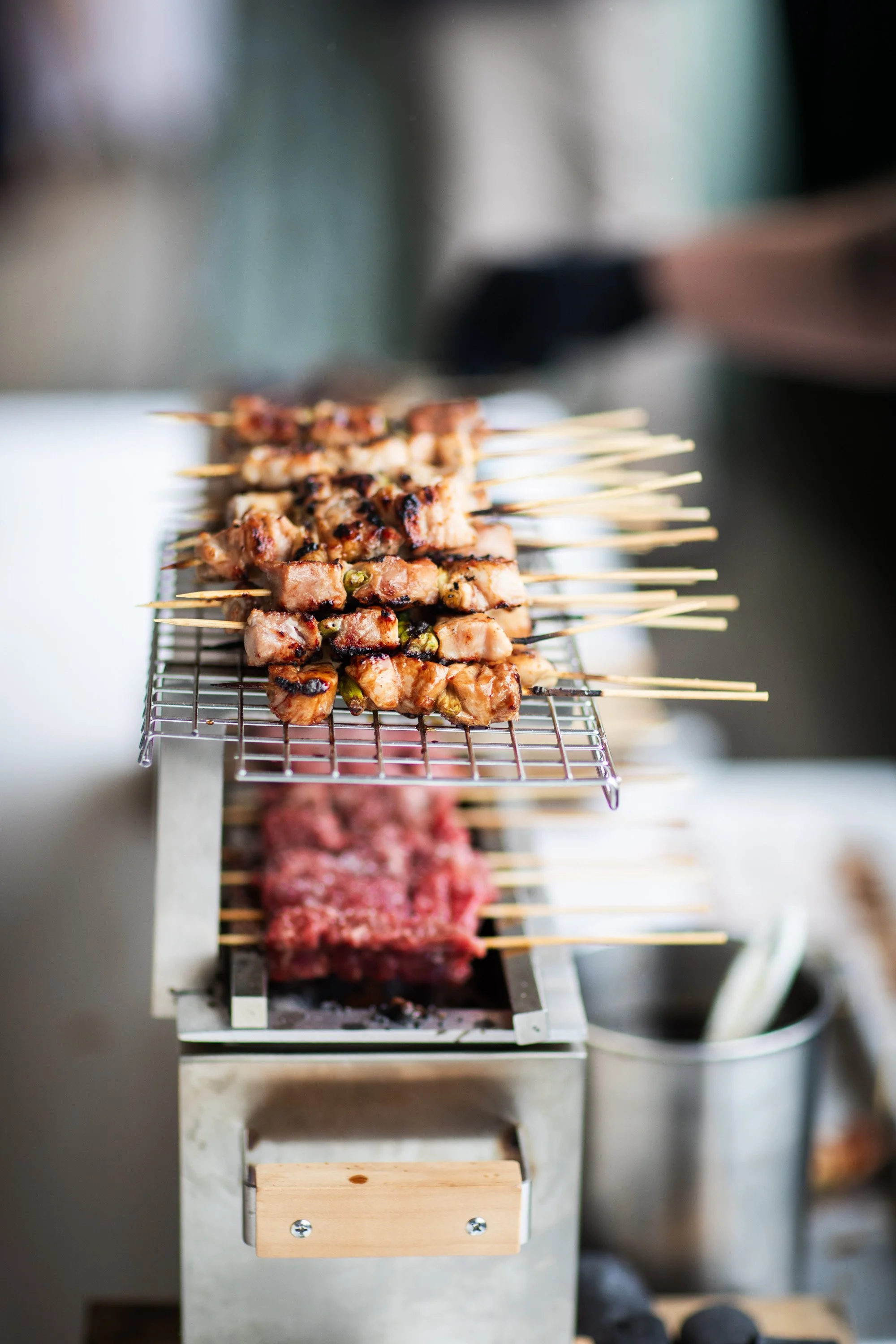 Skewers of grilled meat on a wire rack above a charcoal grill.