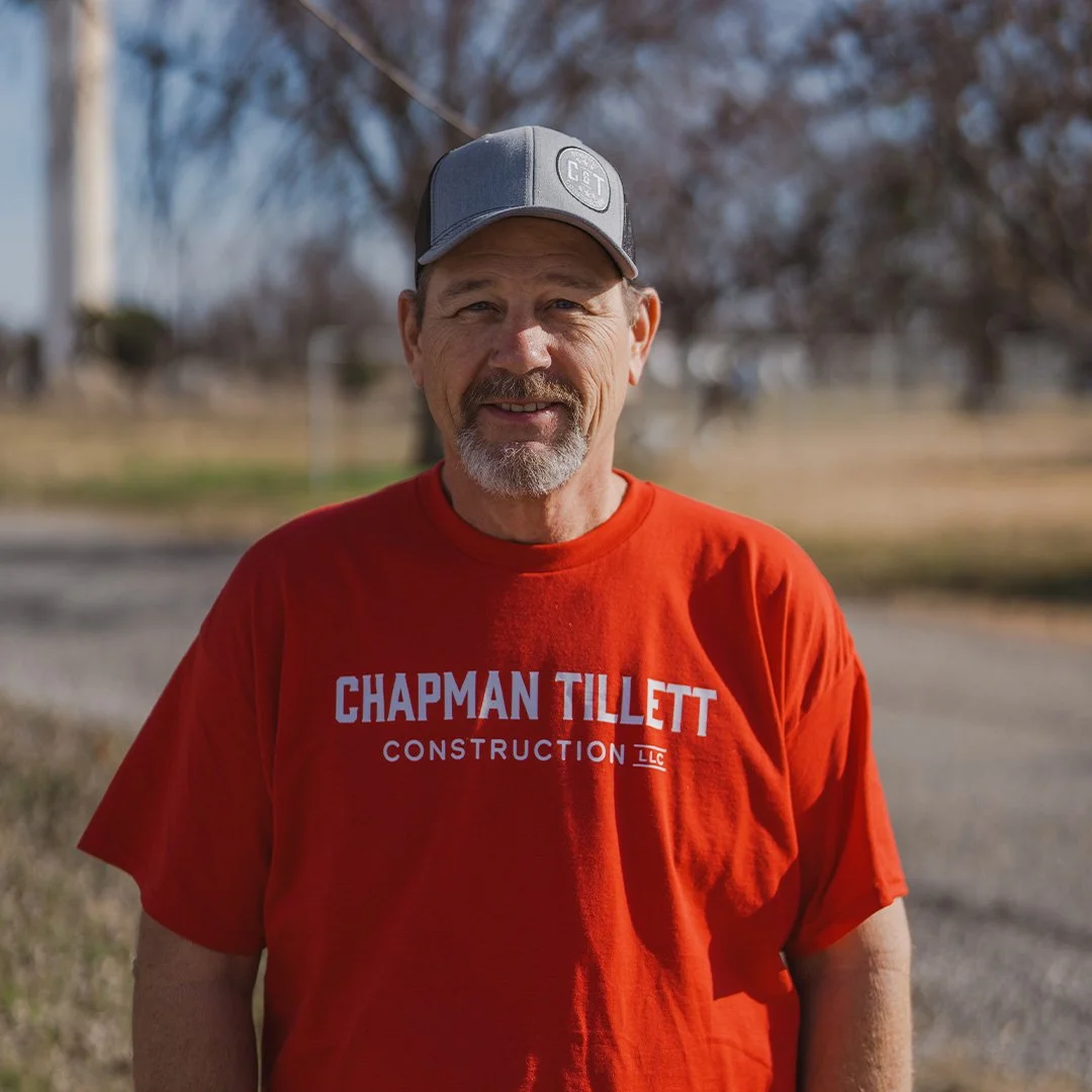 A man in a red shirt and gray hat smiling. 