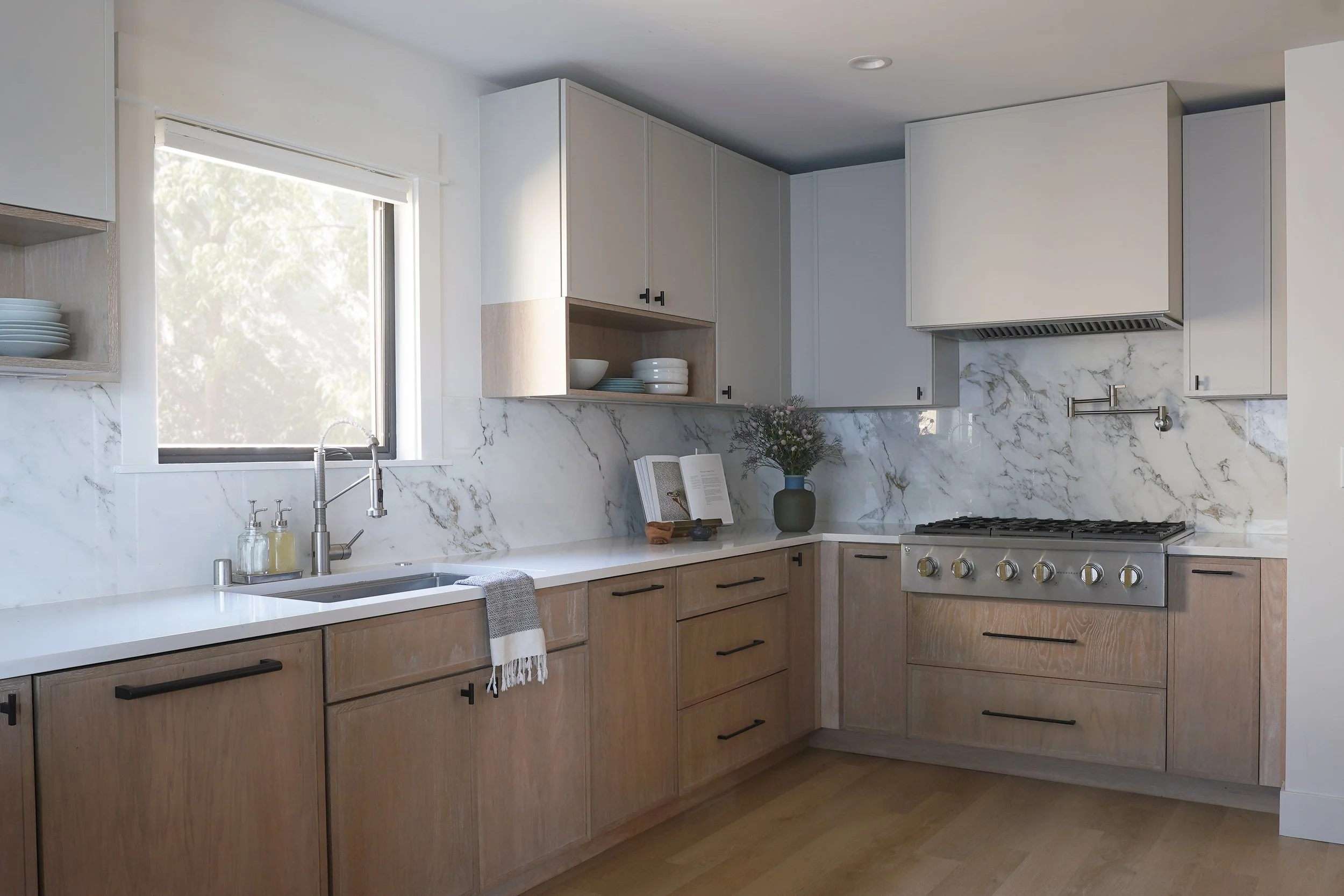 A modern kitchen with wood lower cabinets, white upper cabinets, a marble backsplash, and a white countertop.