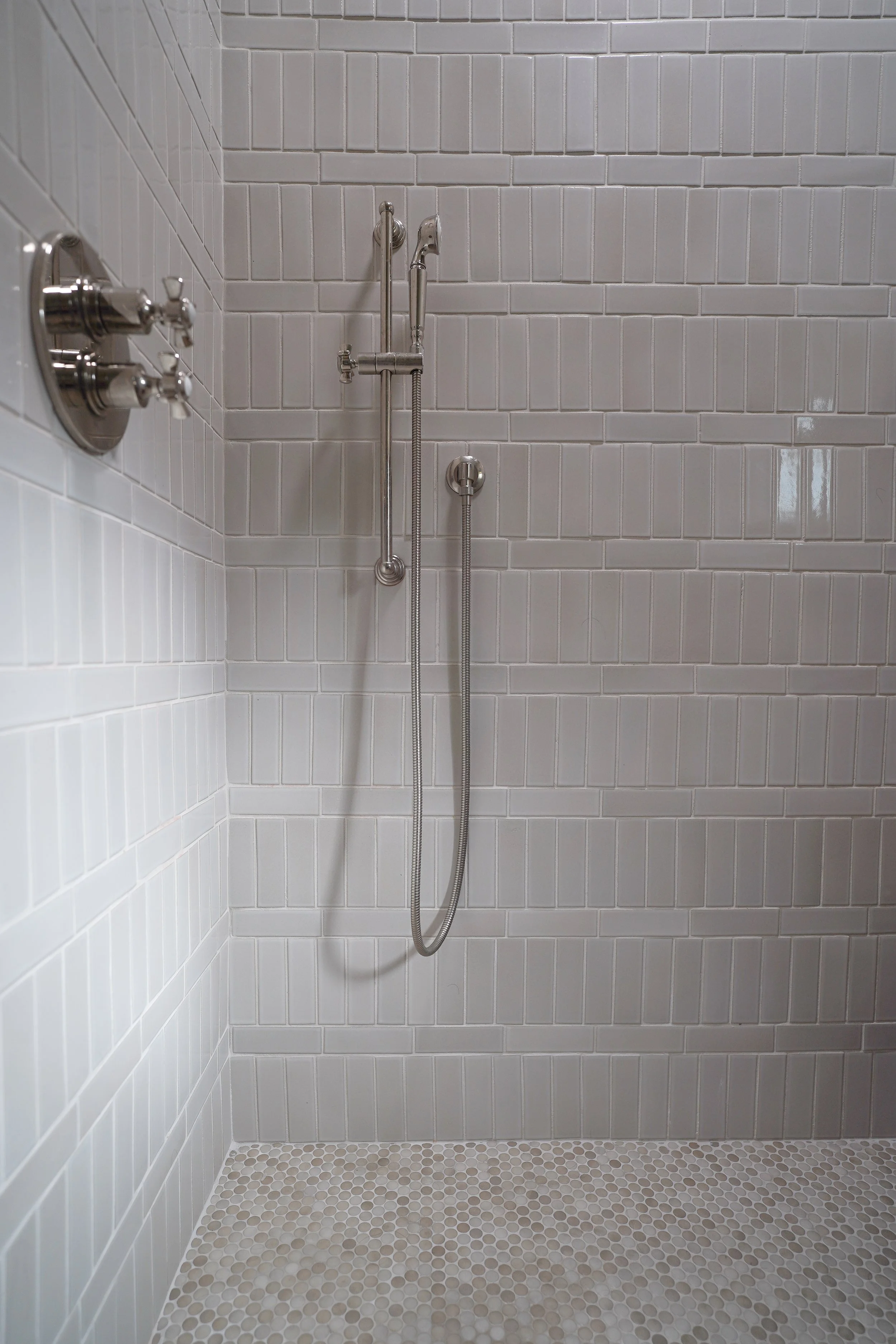 Shower with white subway tile walls, a handheld showerhead, and a hexagonal tile floor in shades of white and beige.
