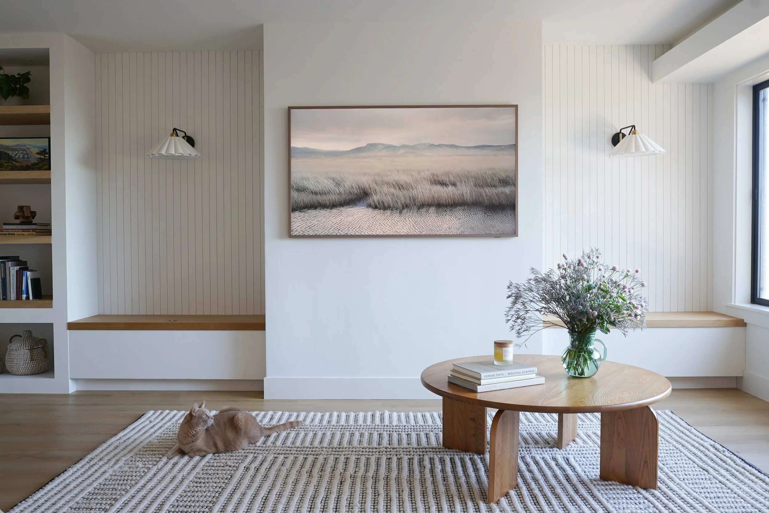 Millbrae Coastal Ranch living room with custom shiplap walls, built-in shelving, round oak coffee table, and landscape art — residential interior design by Kit Studio, Bay Area