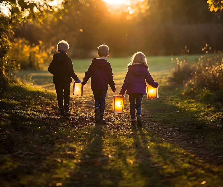Three children walking on a dirt path in a park during sunset, each holding a lantern that illuminates their way.