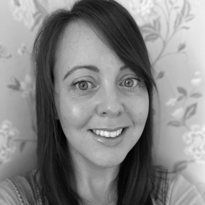 Black-and-white photo of a woman with long dark hair smiling, with floral wallpaper in the background.