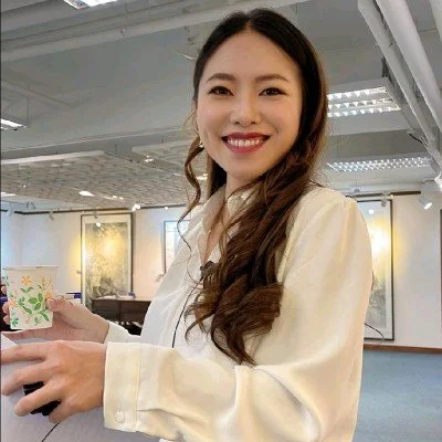 A smiling woman with long brown hair holding a colorful mug in an art gallery or exhibition space.