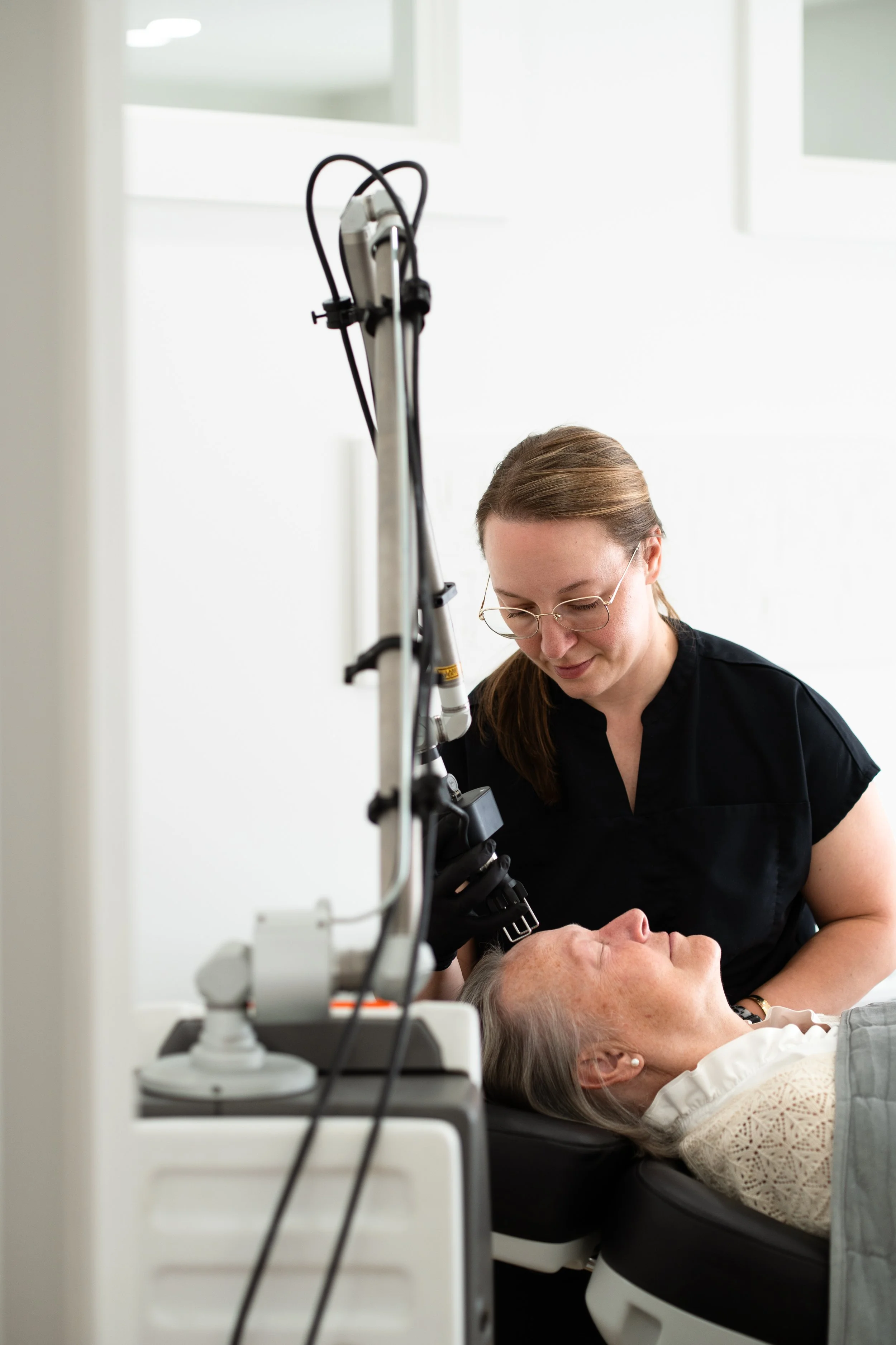 A healthcare professional performing a medical procedure on an elderly woman lying on a medical chair in a clinical setting.