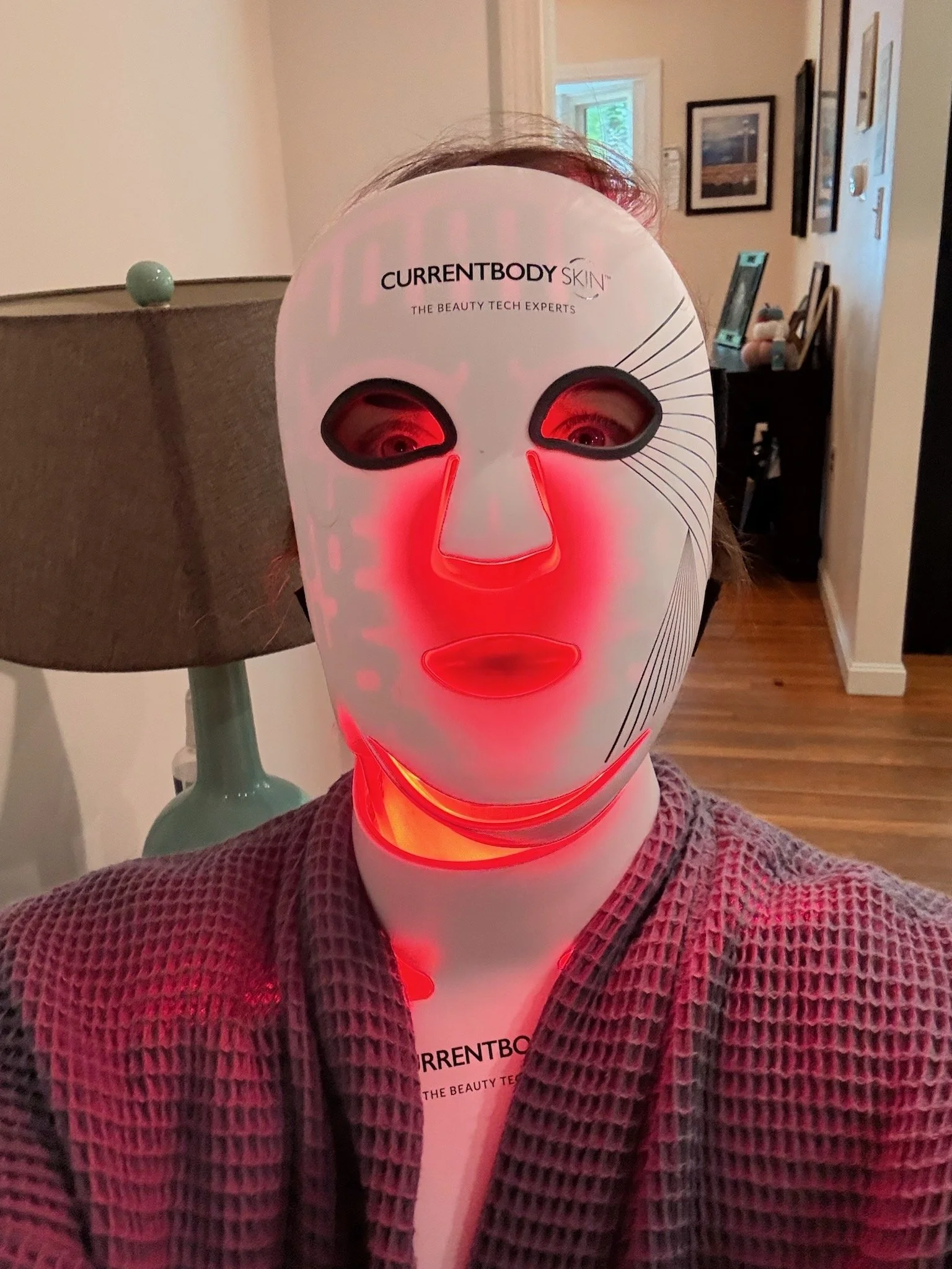 Woman using red light mask at home.