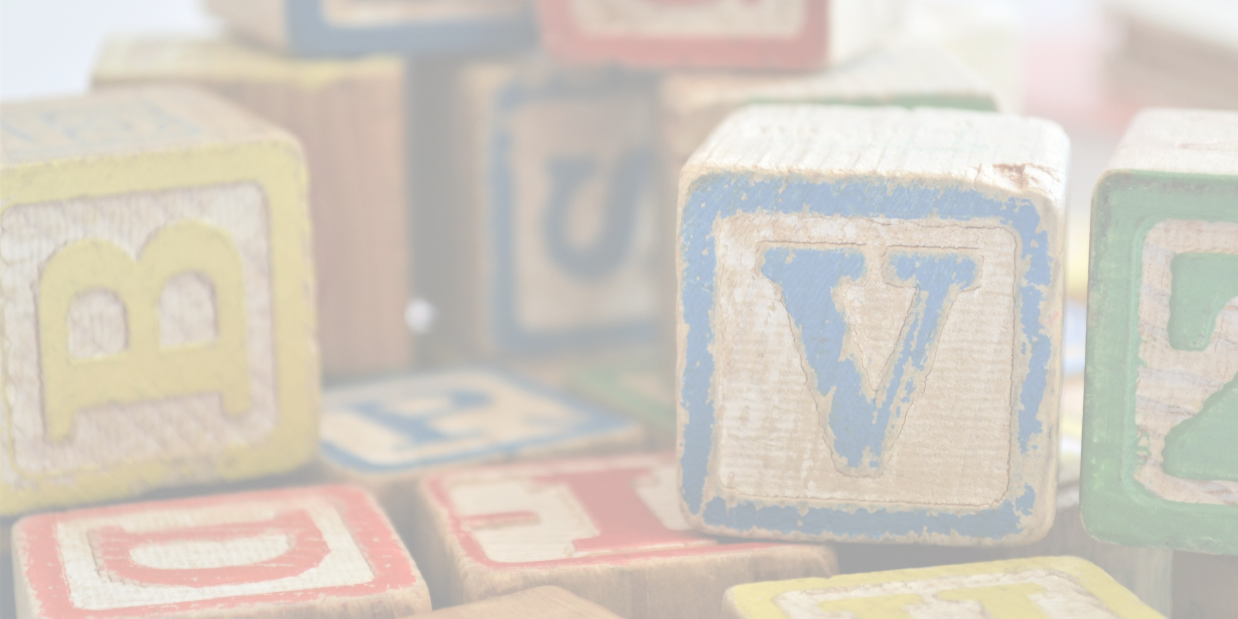 Close-up of worn wooden alphabet blocks, including a blue block with a 'V', among other colorful blocks with letters.