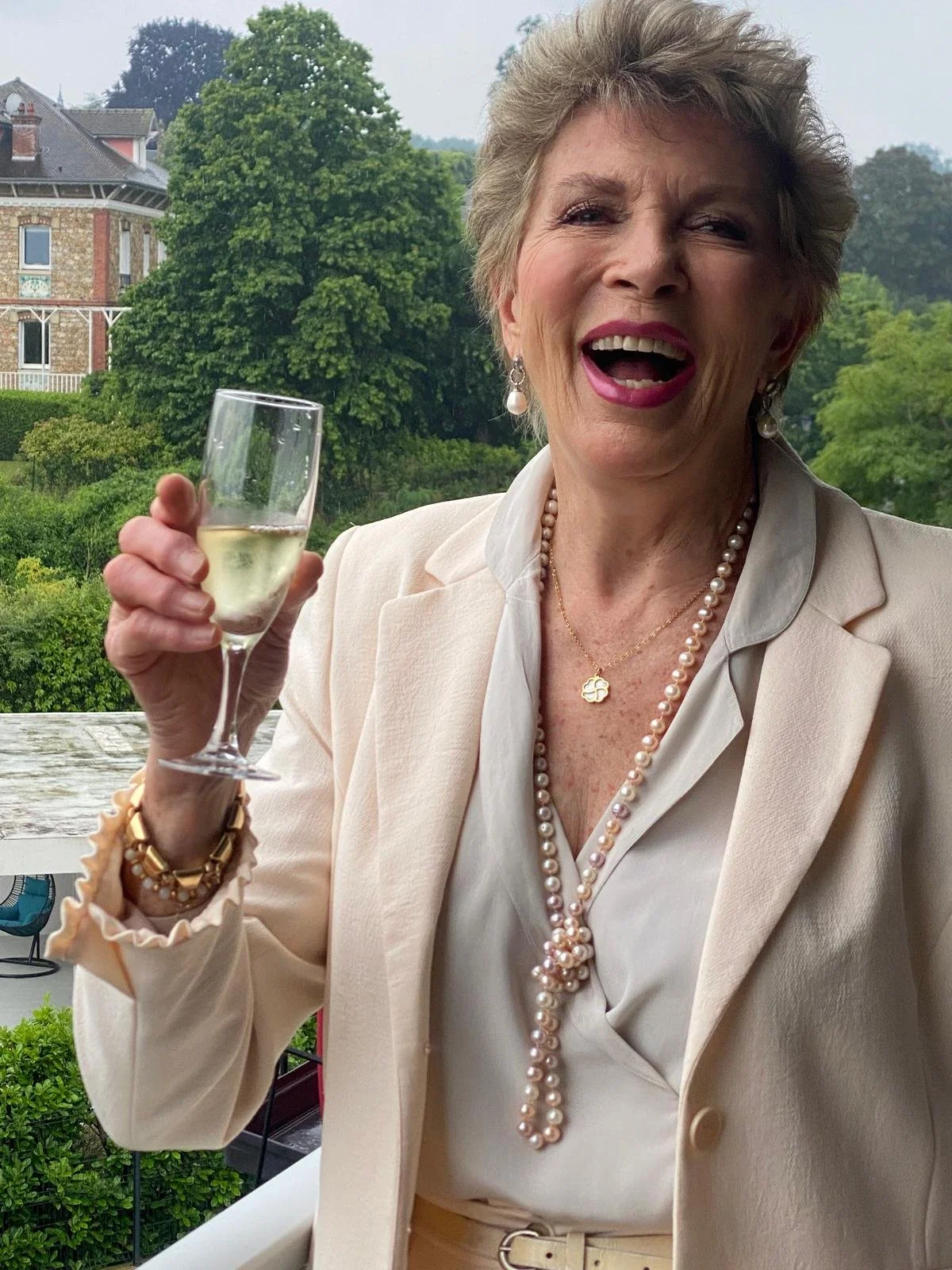 Smiling woman outdoors with short blonde hair and bright red lipstick.