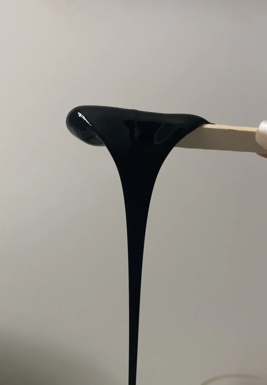 Black sticky substance on a popsicle stick against a plain background.