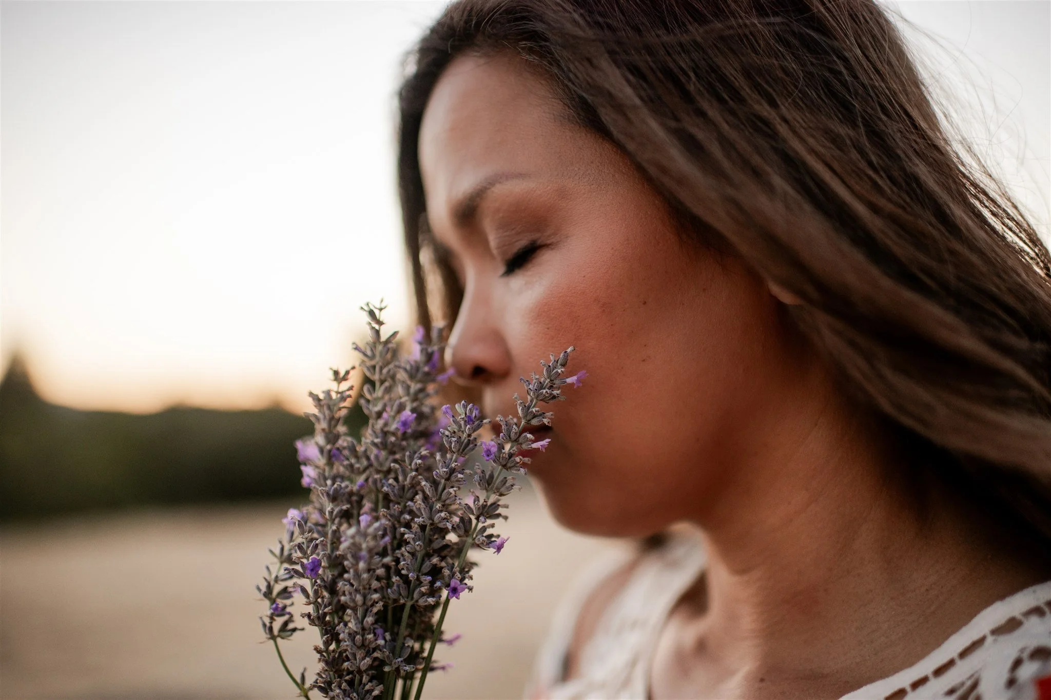 Grace Killpack smelling a bunch of lavender flowers outdoors at sunset.