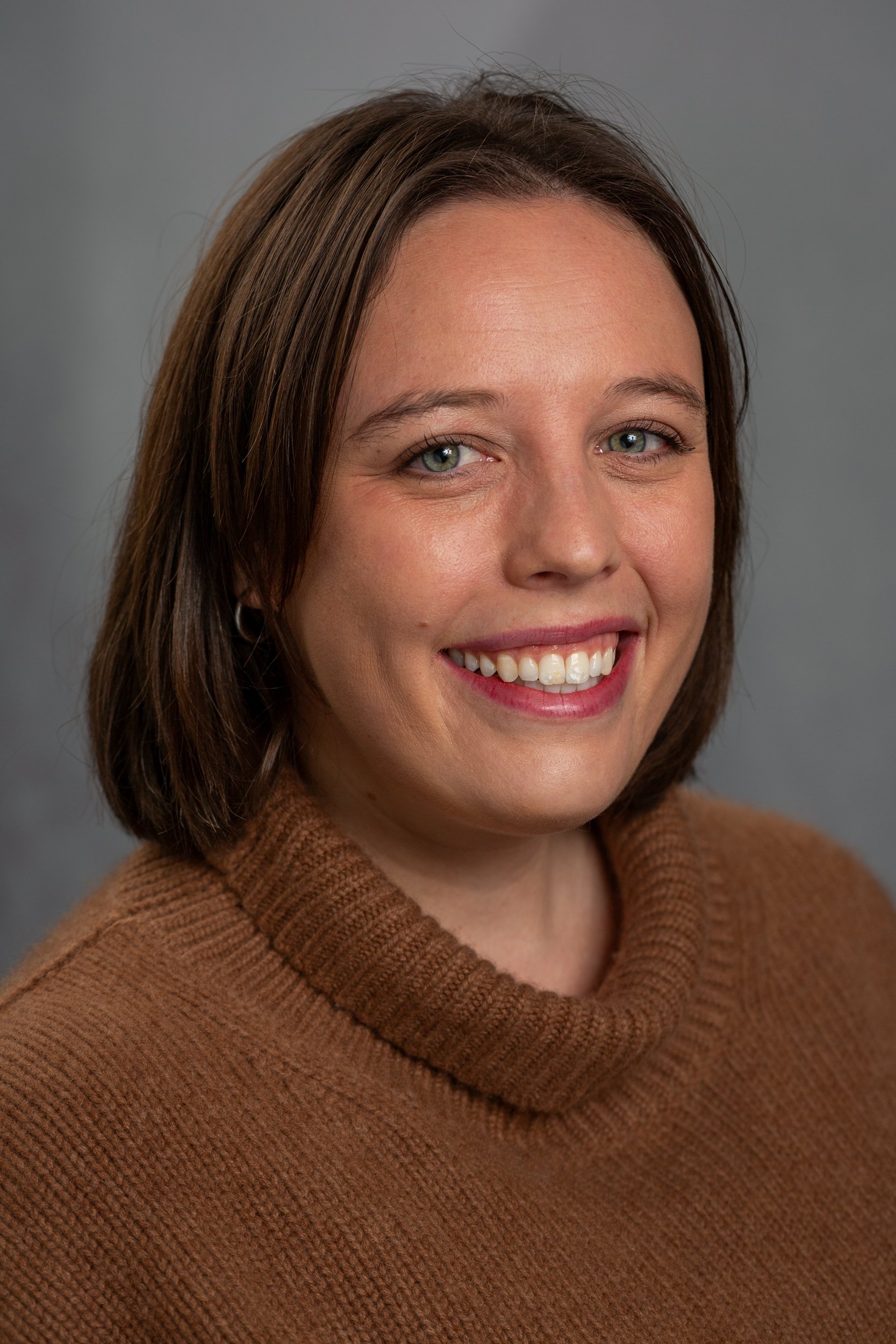 A smiling woman with short brown hair wearing a brown turtleneck sweater.