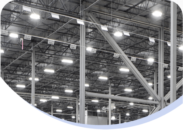 Interior view of a large warehouse or industrial facility with metal beams, bright overhead lighting, and rows of shelving or equipment.