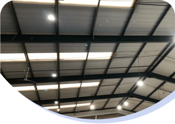 Indoor ceiling with metal beams, overhead lights, and panels in an industrial or warehouse setting.