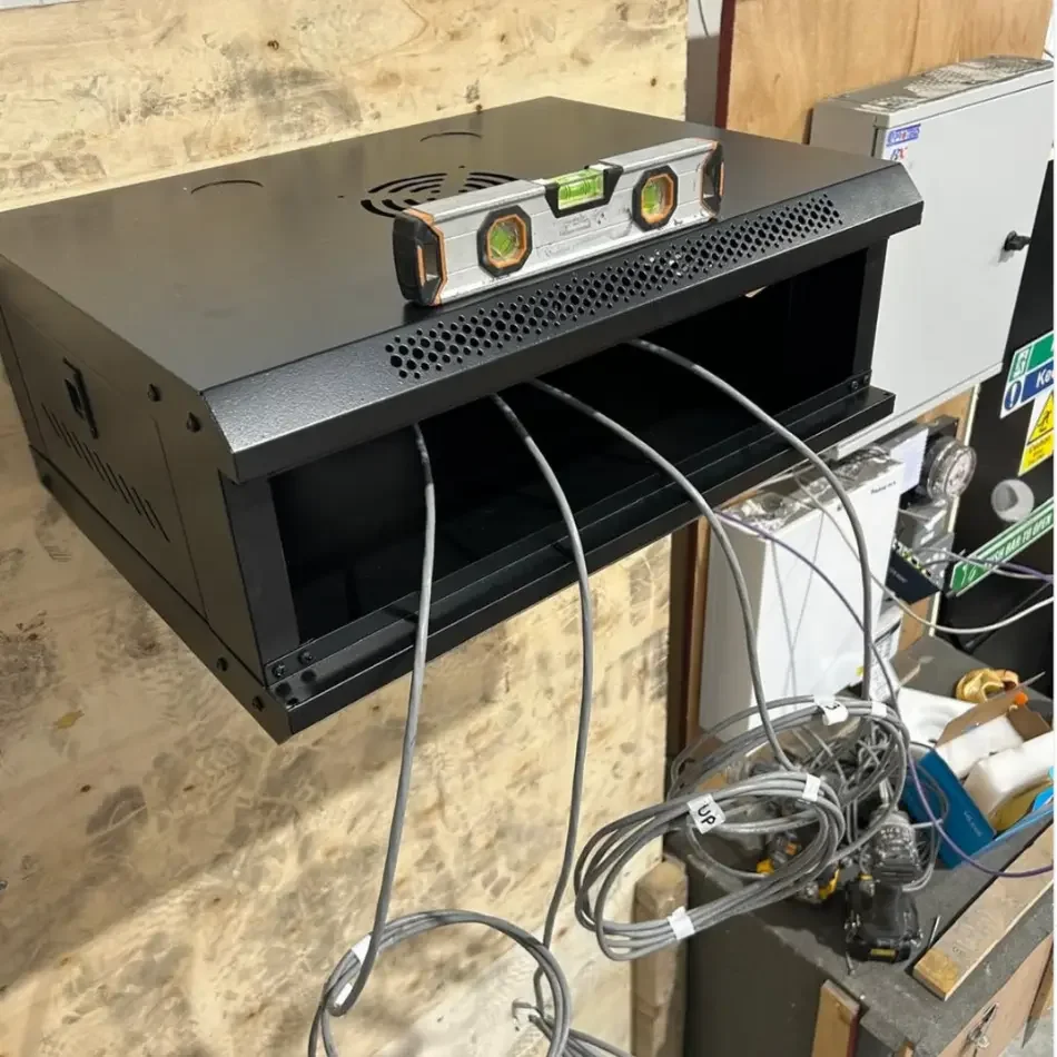 A black electronic device with a level and three cables connected to it, set on a wall-mounted shelf in a workshop.