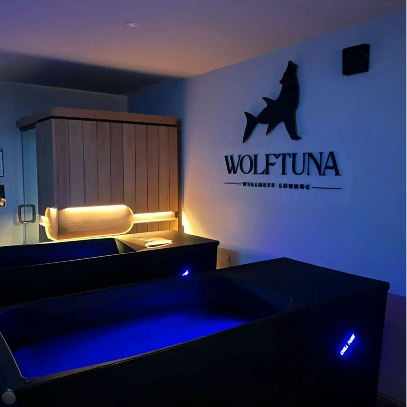 Interior of Wolftuna Wellness Lounge with illuminated blue tanning beds and a wall sign featuring a wolf silhouette and the lounge's name.