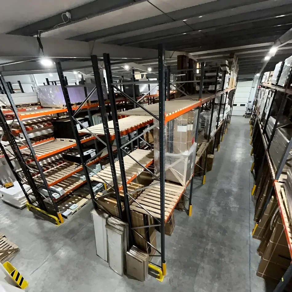 Warehouse storage area with metal shelving units filled with boxes, pallets and supplies, seen from an elevated angle.