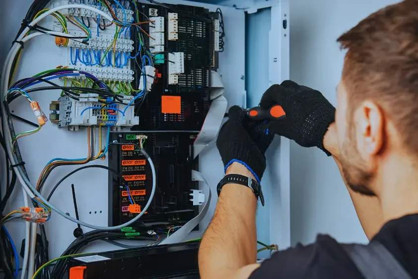 Technician working on an electrical control panel with various wires, circuit boards, and components.