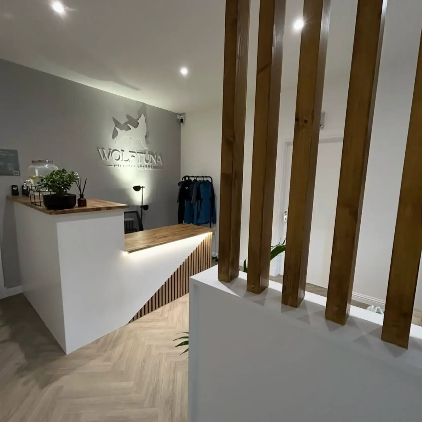 Interior of a modern office or reception area with a white and wooden reception desk, a wooden partition, and a sign that reads 'WOLF & TUNA'.