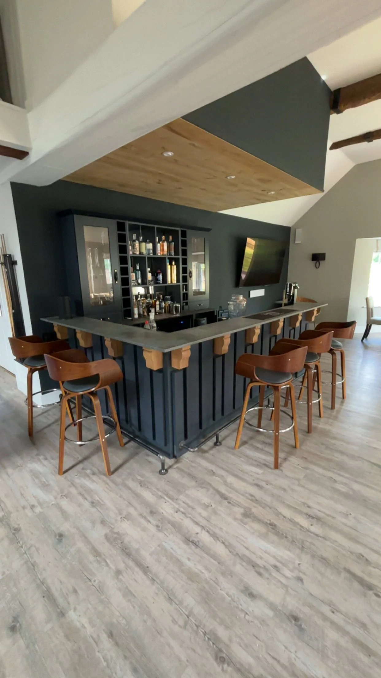 Modern indoor bar with black cabinetry, a grey and wooden bar top, and brown bar stools with black cushions by CloudNine Construction, Surrey, UK