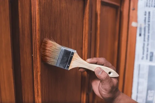 A person painting a wooden surface with a paintbrush.