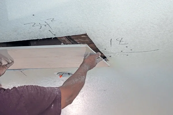 A person installing an opening in a drywall ceiling, with the drywall partially cut out and held in place.