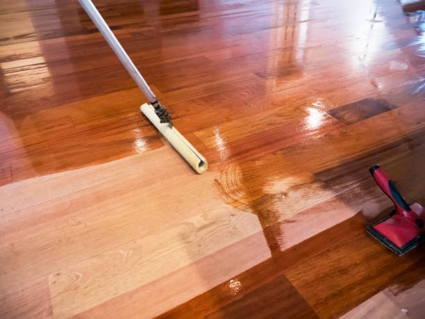 A mop and a floor sander used for refinishing a hardwood floor with different shades of wood stain.