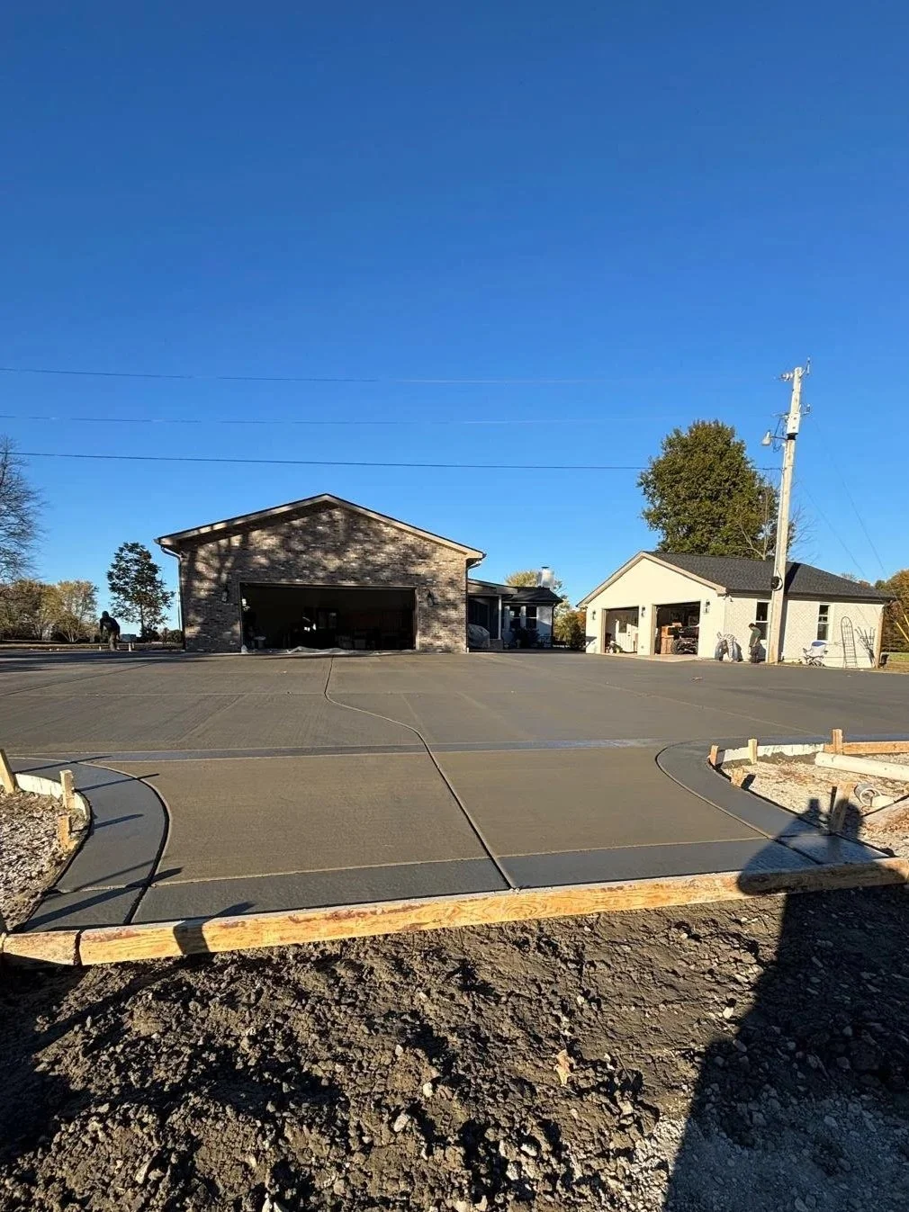A newly poured concrete driveway leading to two detached garages in a residential area under a clear blue sky.