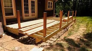 Wooden deck framing under construction next to a house in a backyard.
