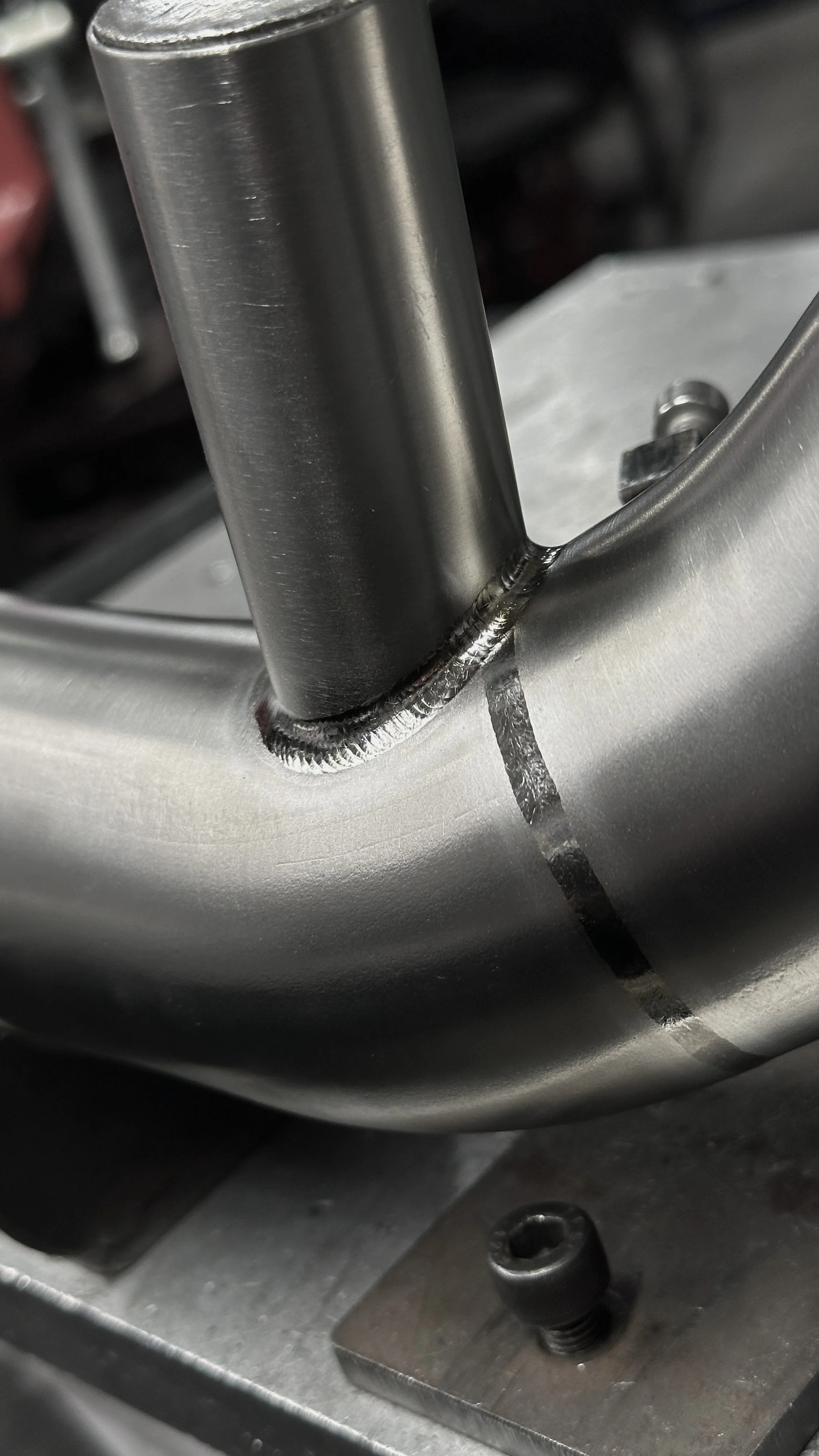Close-up of a metal bicycle fork with weld joint at the crown, mounted on a workbench.