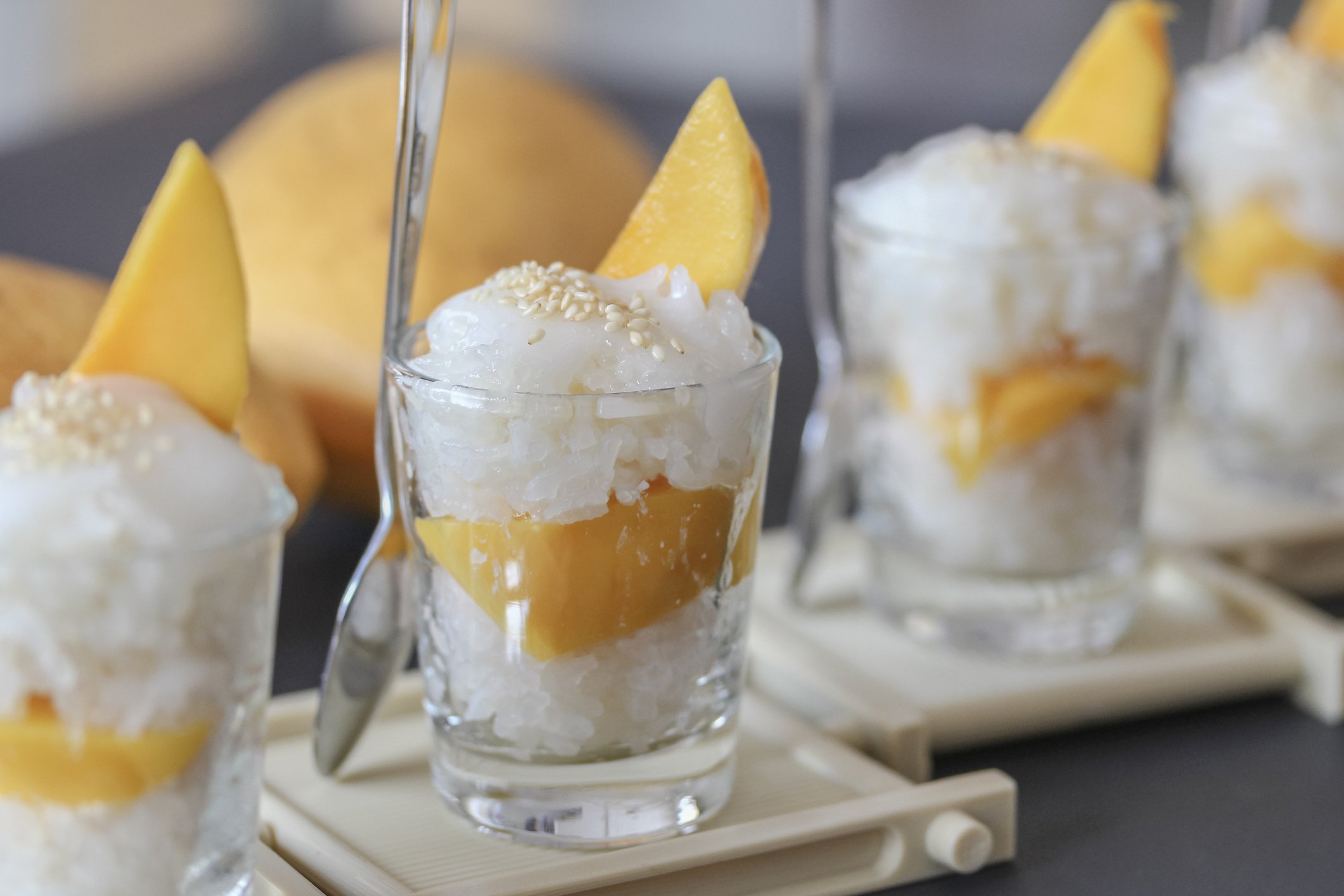 Close-up of three glass cups filled with mango and coconut dessert topped with coconut flakes and mango slices.