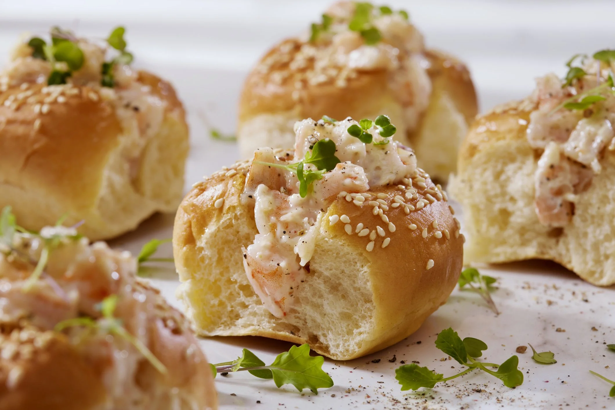 Cream cheese stuffed bread balls garnished with microgreens and sesame seeds on a white surface.