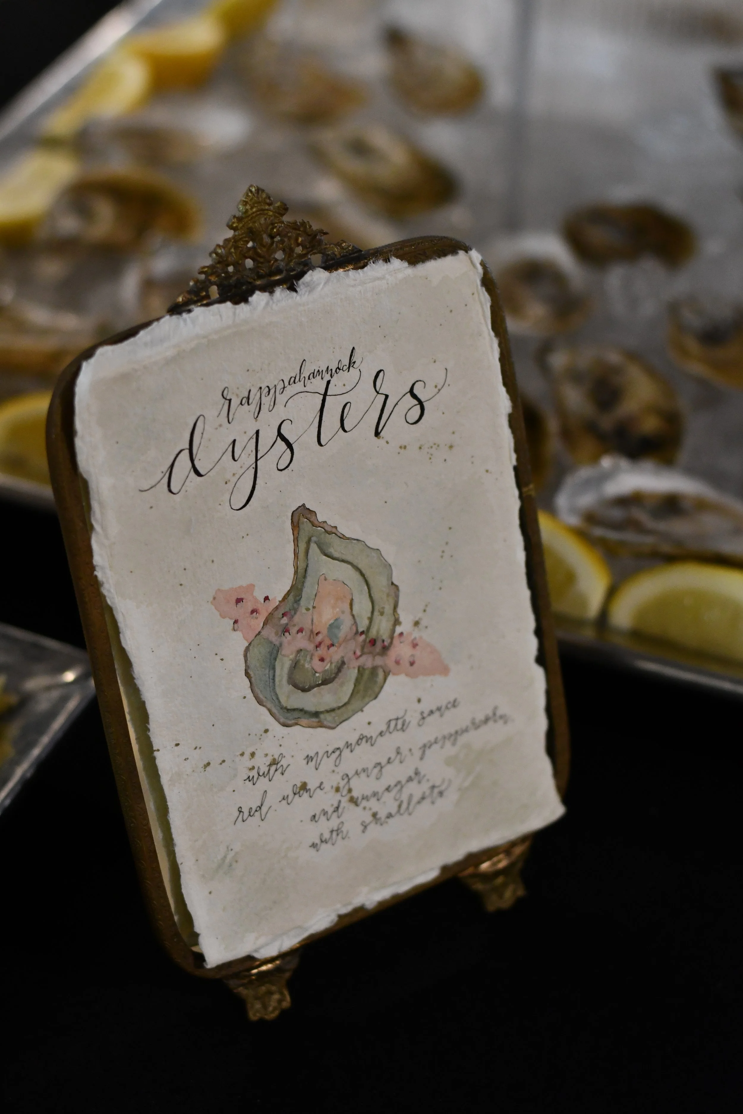 Display sign for Rappahannock oysters, with a watercolor illustration of an oyster and description of ingredients, surrounded by trays of lemon wedges and oysters.