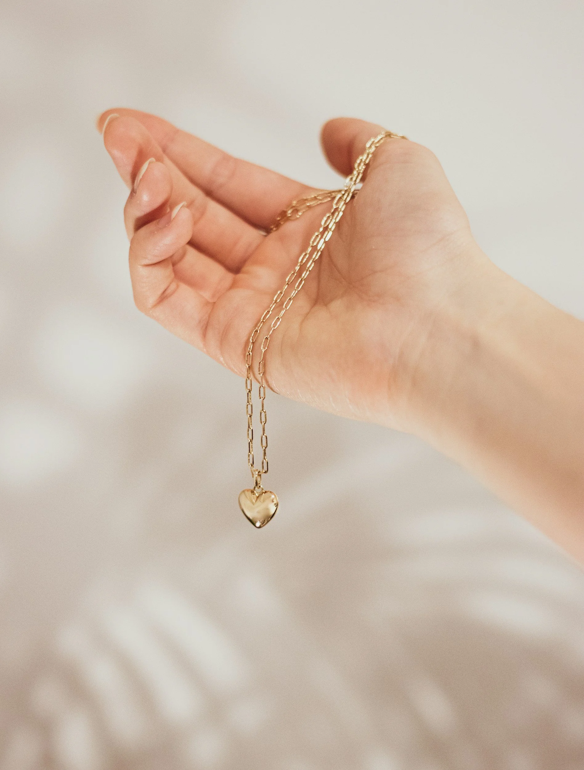 Hand holding gold chain with light grey background