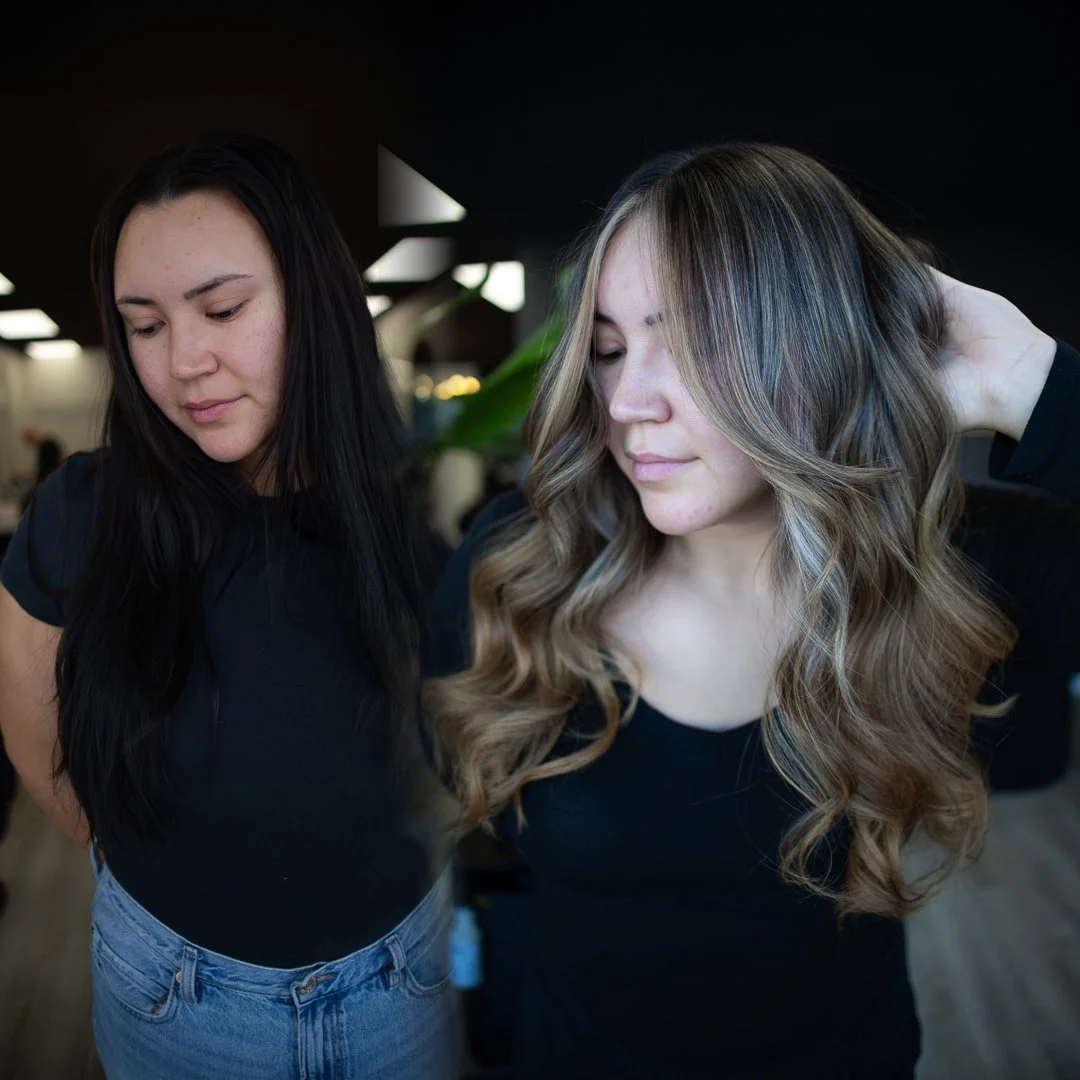 Two women with dark and light brown hair in black tops, standing close together in an indoor setting.