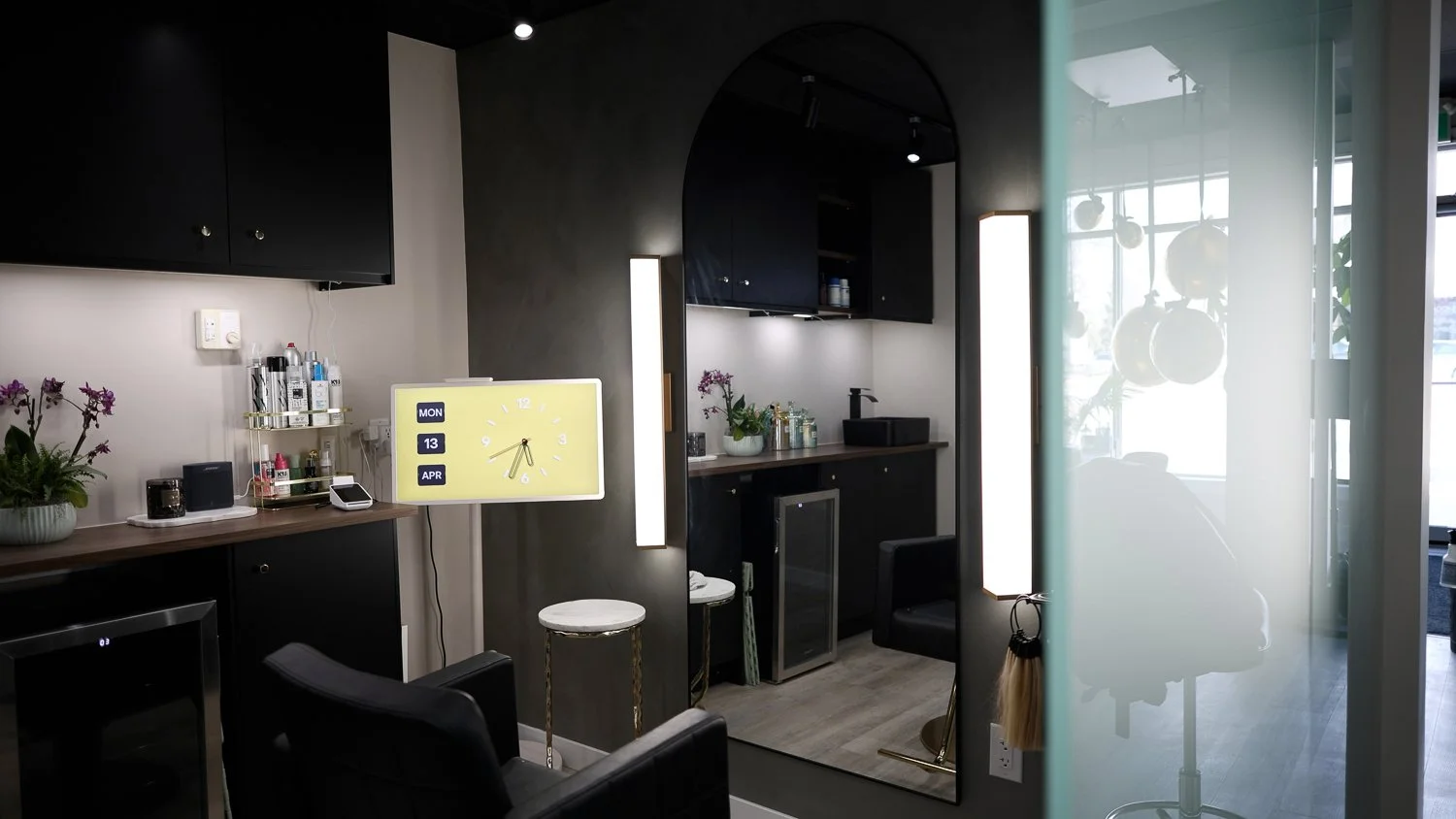 Interior of a modern kitchen with dark cabinets, a mirror, and various kitchen items, viewed through a glass panel.
