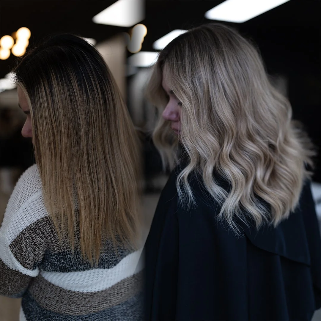 Two women with styled blonde hair standing side by side in an indoor setting with dark ceiling lighting.