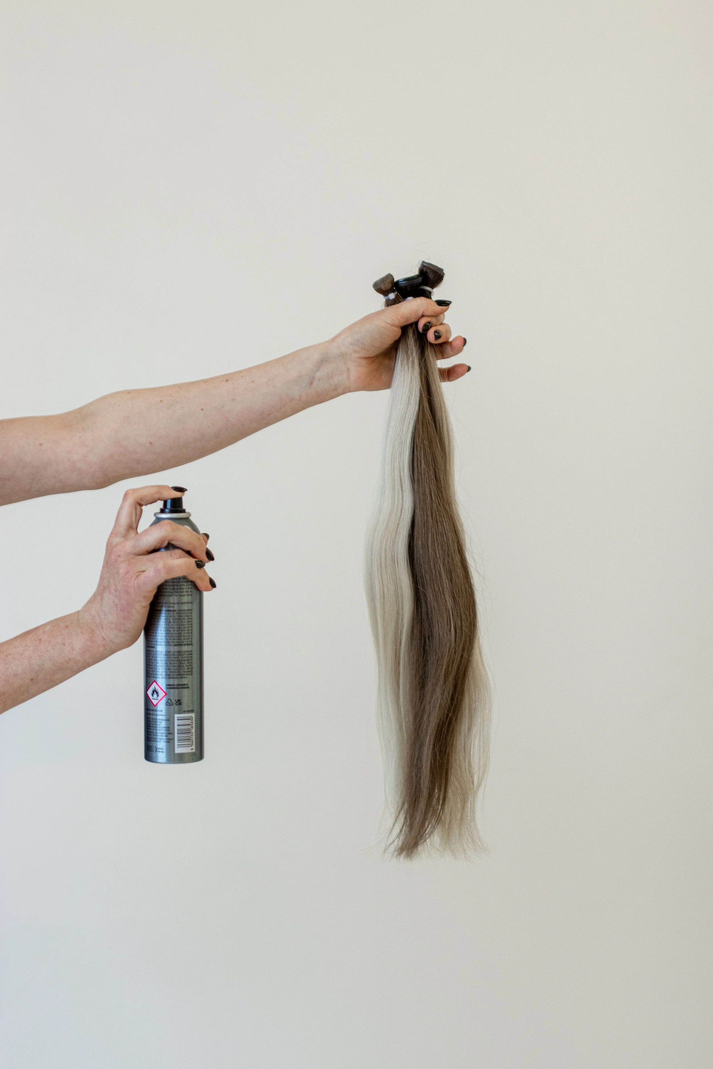 Person holding a hair color spray can and a lock of styled hair against a plain background.