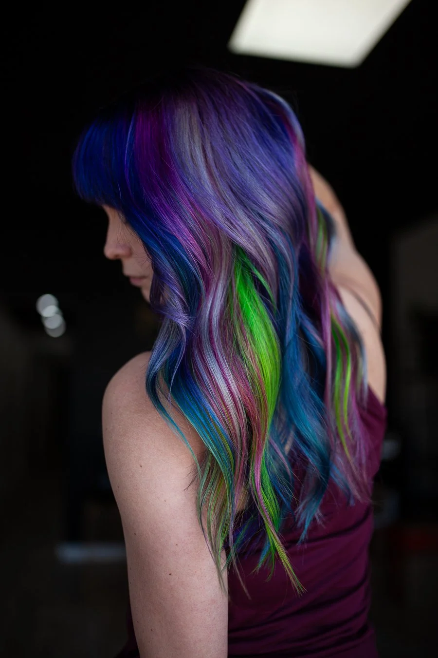 Side view of a woman with long, wavy hair dyed in vibrant rainbow colors including purple, blue, green, and pink.
