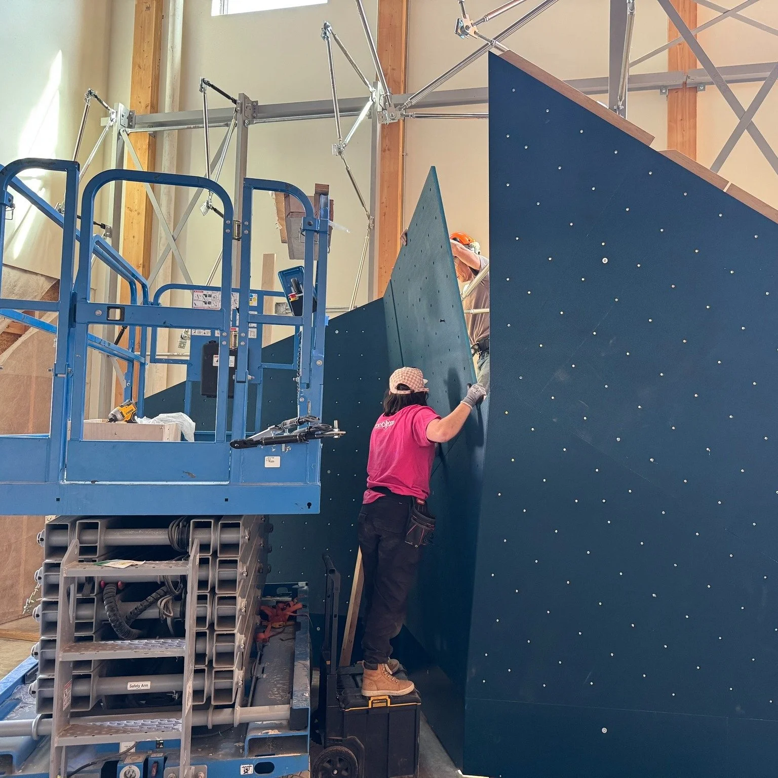 A builder installing the lower climbing-wall panels at Methow Spires in June 2026.