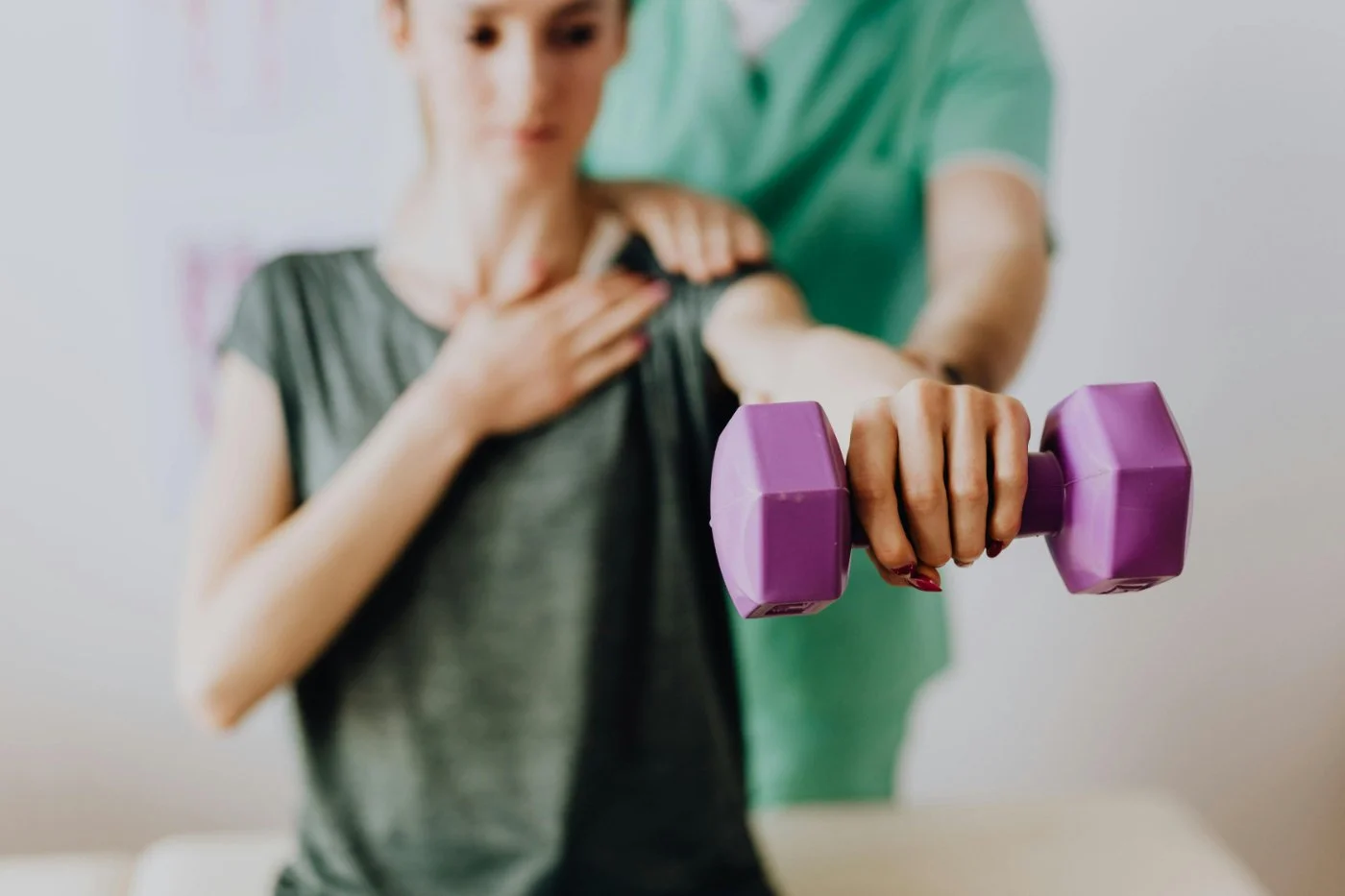 A woman is receiving guided support from a physical therapist while she exercises with a purple dumbbell.