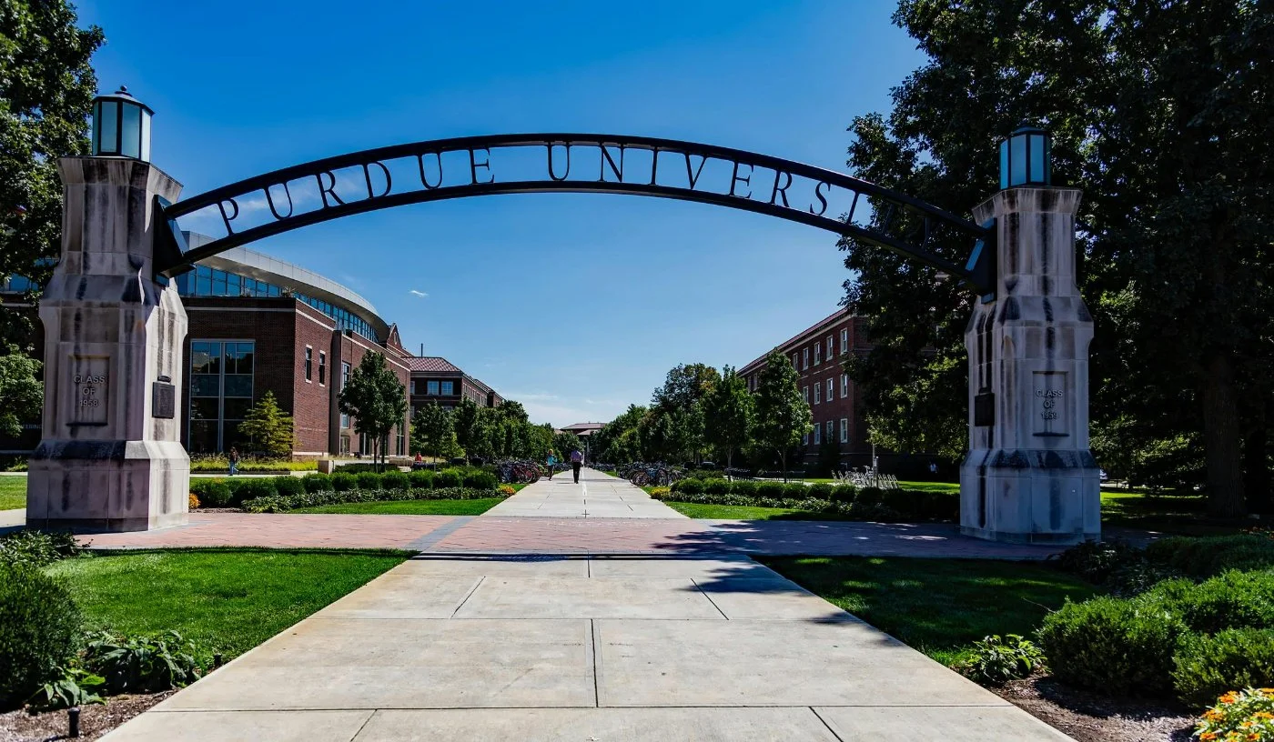 Purdue University entrance archway on a sunny day with trees and campus buildings in the background.