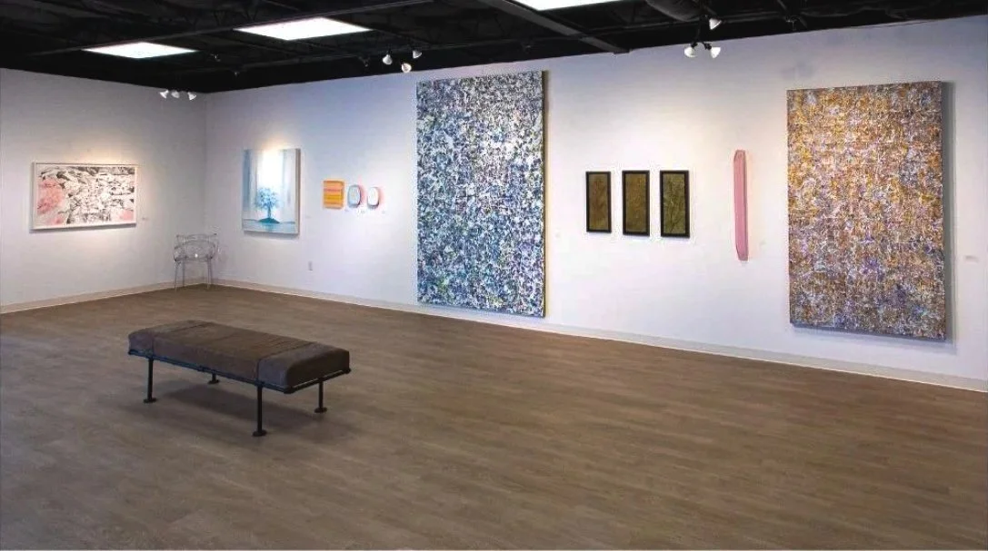 Art gallery with various paintings on white walls and a bench in the center.