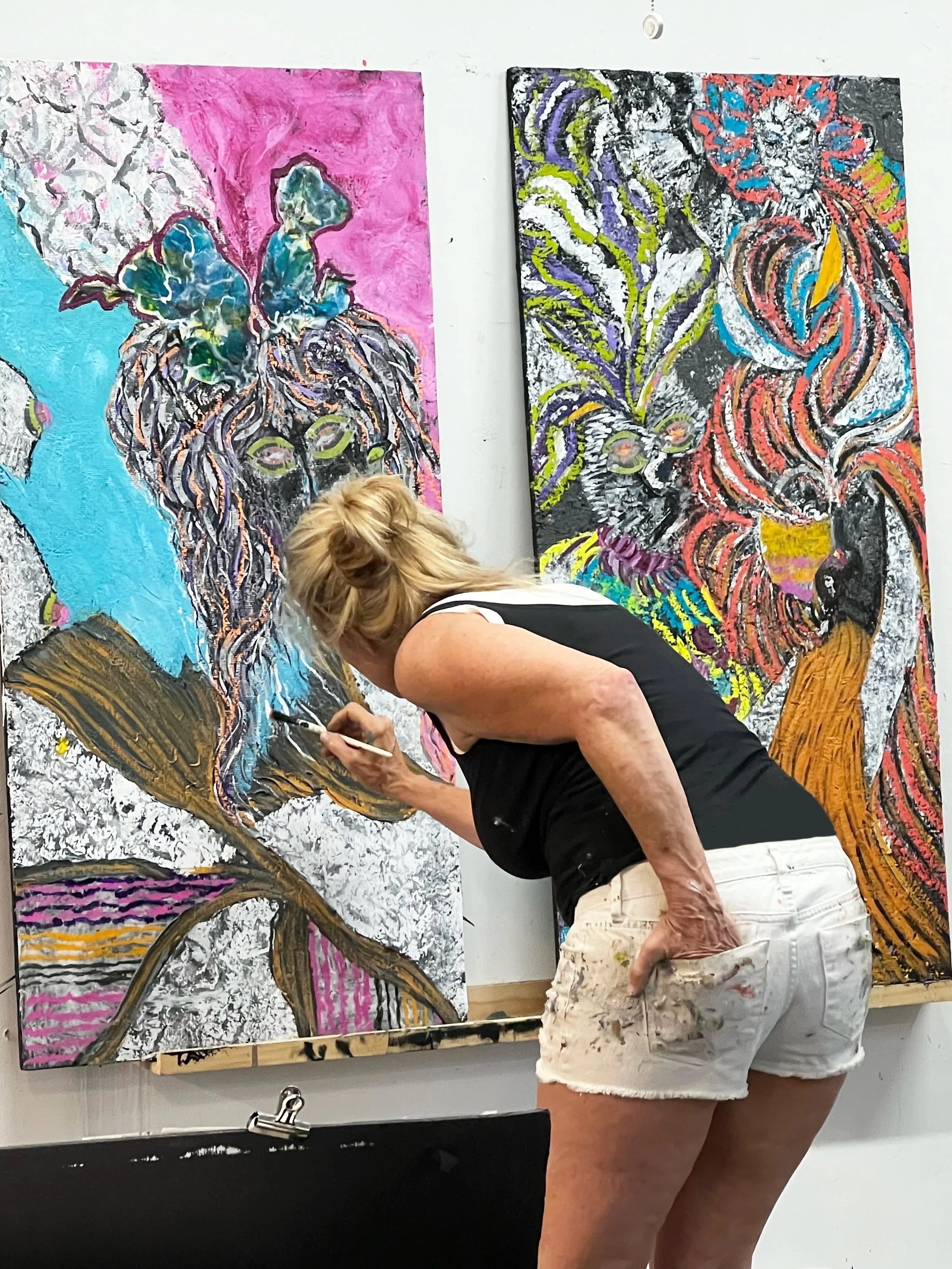 An artist painting colorful, abstract animal portraits on two large canvases in a studio.