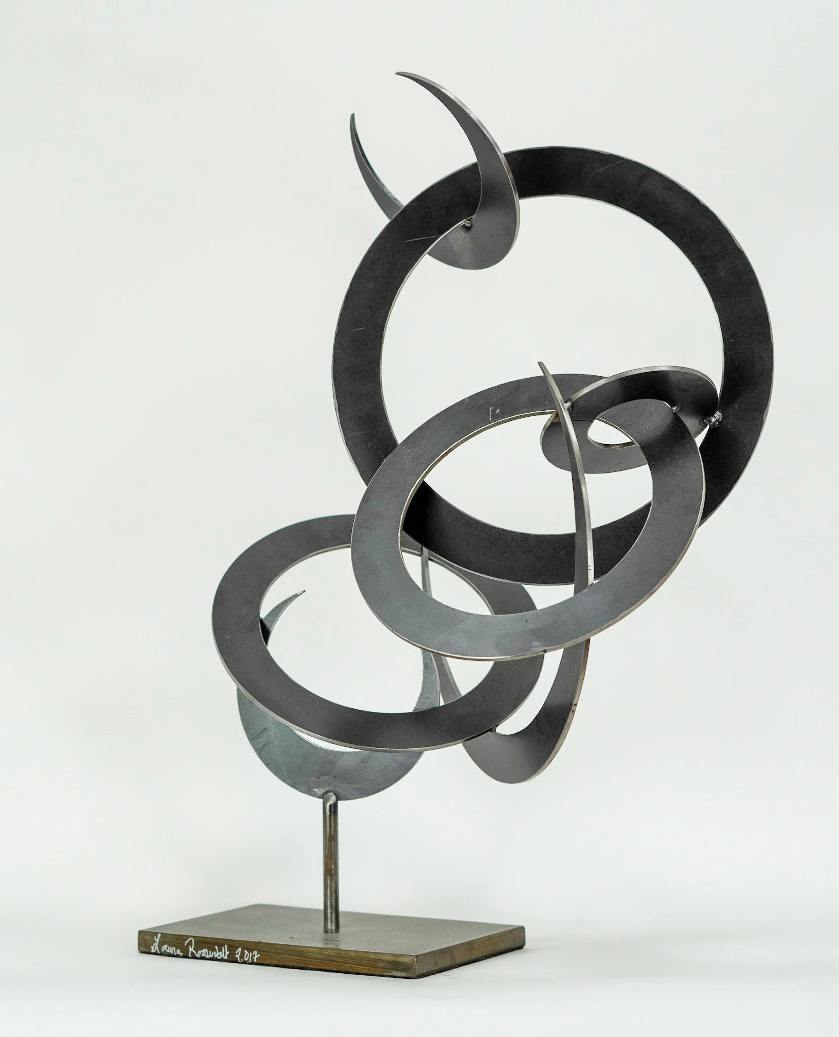 Abstract metal sculpture with intertwined circular and curved elements on a gray stand.