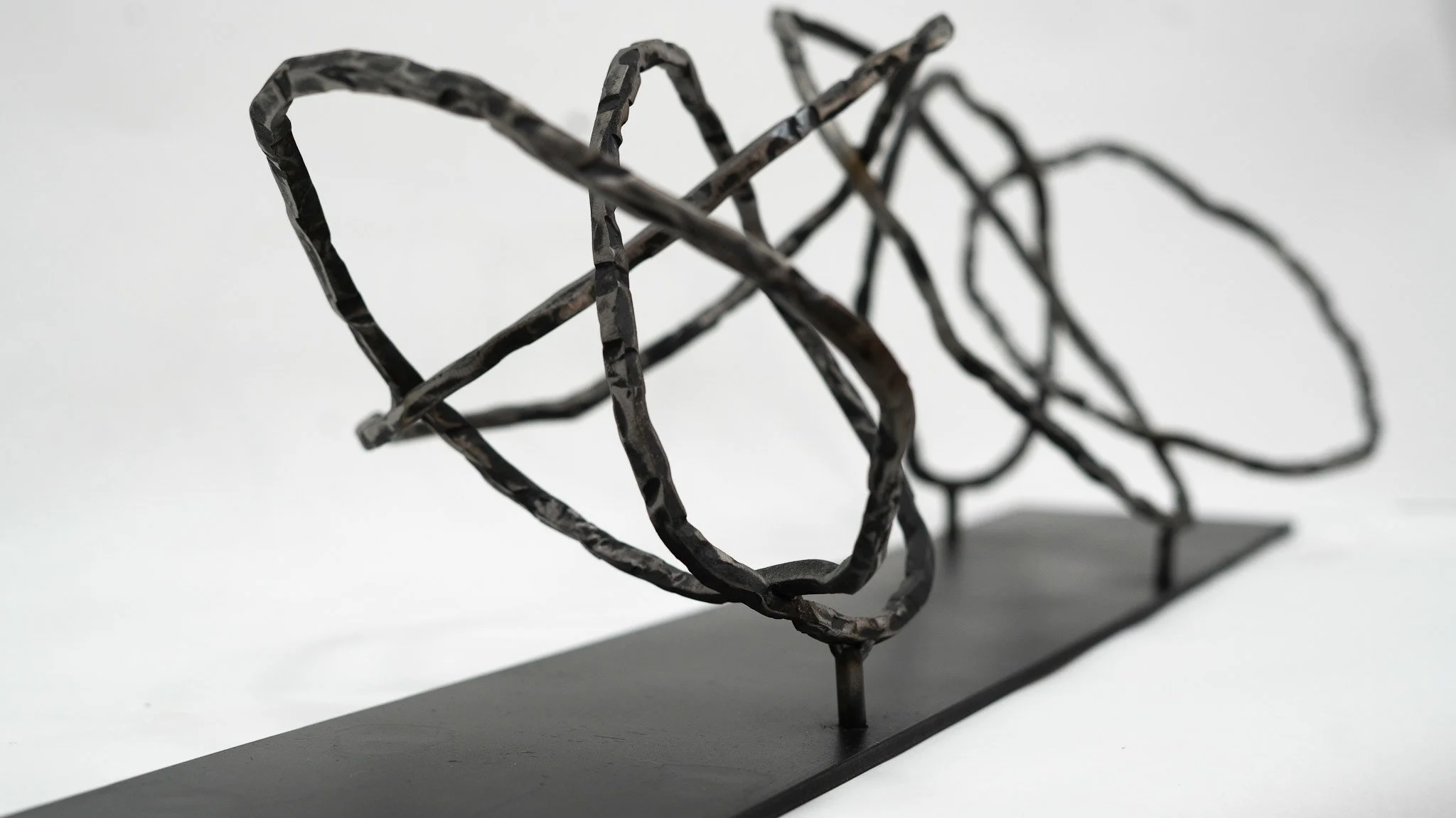 Abstract black metal sculpture on a black base, resembling intertwined loops and shapes.