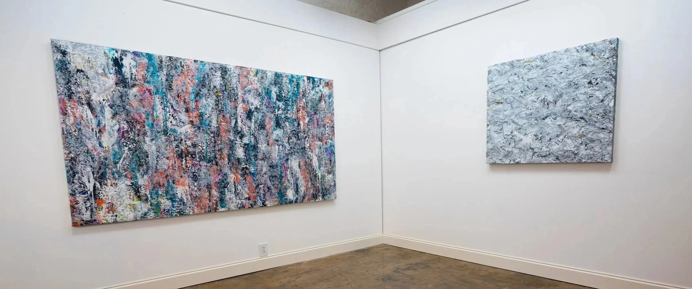 Two abstract paintings hanging on a white gallery wall, with one large, colorful piece on the left and a smaller, gray-toned piece on the right.