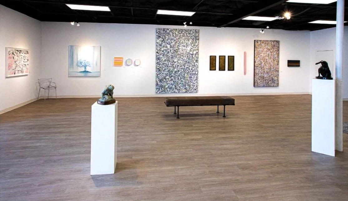 Empty art gallery with various paintings and sculptures on display, and a bench in the center.