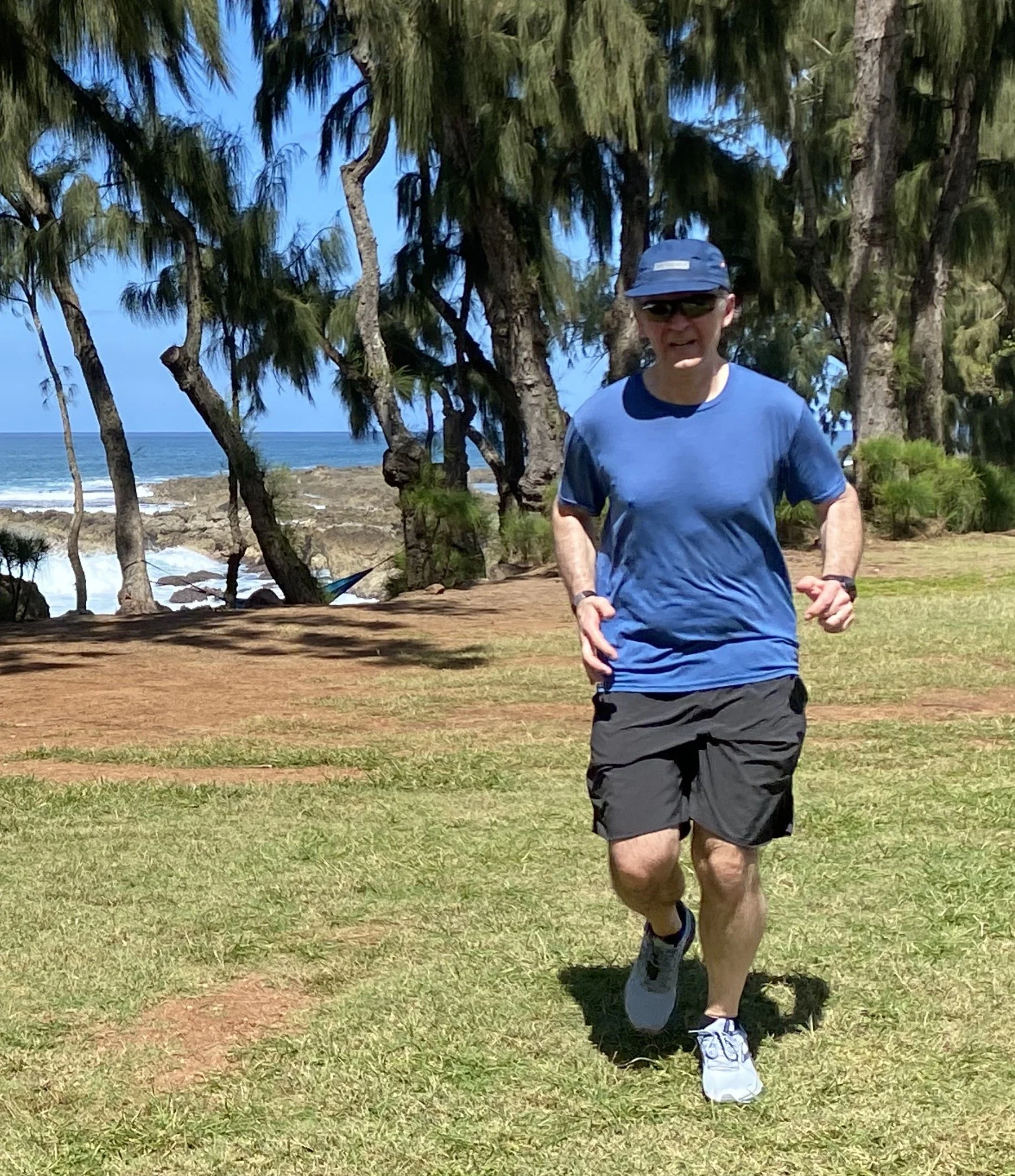 A man jogging on a grassy area near a beach with palm trees and ocean in the background.