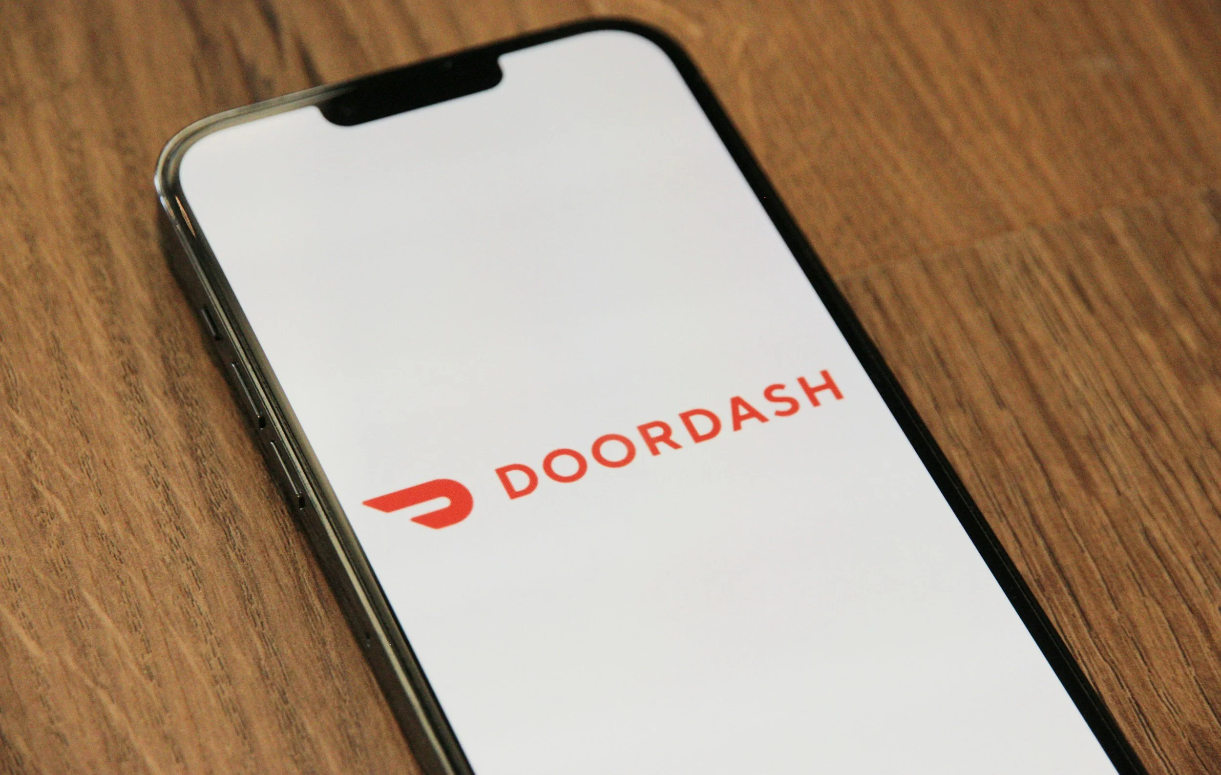 Smartphone displaying the DoorDash app logo on a wooden surface.